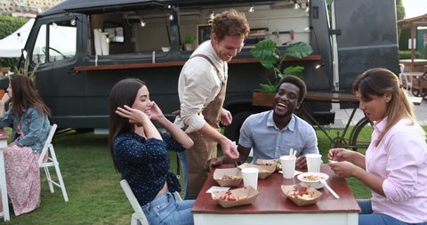 Multiracial friends eating at food truck table outdoor - Summer and lifestyle concept