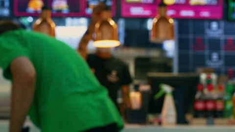 In blur. A fast food restaurant with a cashier behind the cash register, a delivery man in a green T-shirt, collecting an order in a paper bag. Takeaway food, home delivery.