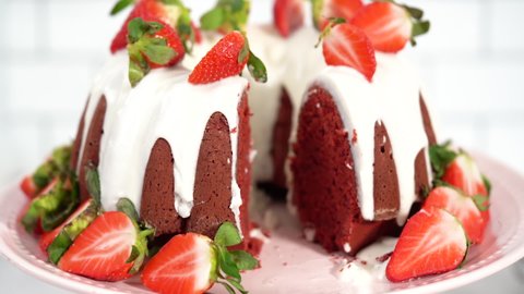 Step by step. Slicing red velvet bundt cake with cream cheese frosting garnished with fresh strawberries.