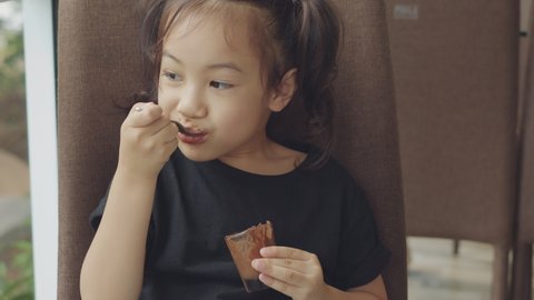 Close up portrait 4K of adorable 5 years old asian girl with black hair is eating sweet chocolate moose with happy, enjoy and funny emotion and express tasty and delicious shows dirty mouth.