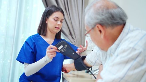 Asian young woman nurse at nursing home taking care of senior elderly man sit on sofa. Caregiver Therapist doctor examining an older patient use blood pressure gauge. Medical insurance service concept