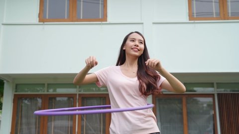 Asian Beautiful young woman doing cardio workout, rotating hula hoop in garden at house. Happy attractive girl enjoy free leisure activity exercise to loss weight for healthcare and well being at home