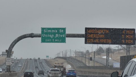 Denver , Colorado , United States - 01 25 2021: Traffic on Interstate Highway Under Snowfall in Cold Winter Day, Vehicles, Exit Road Sign and Display Board, Slow Motion