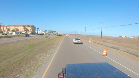 Roof top view of vehicle while driving into road construction zone with orange barrels on a sunny day; driving from North Padre Island near Corpus Christi Texas USA