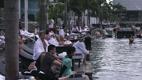 Singapore , Southeast Asia , Singapore - 02 28 2019: Tourist guests resting on Lounge Chairs by the edge of infinity Pool at Marina Bay Sands