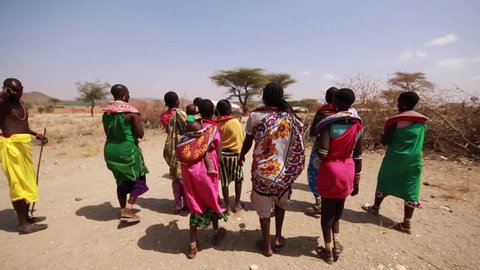 Narok , Kenya - 01 23 2021: POV walking along with Maasai local tribe in traditional colorful clothing through small village in the drylands of Maasai Mara National Reserve