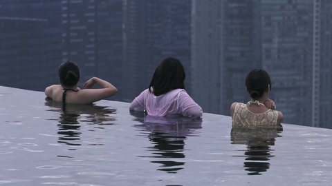 Singapore , singapore , Singapore - 02 28 2019: Tourist Women gazing at Urban Landscape from edge of infinity Pool at Marina Bay Sands Hotel