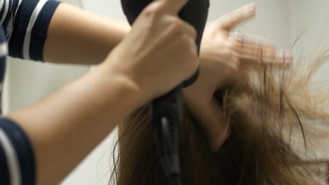 Hairdresser blow drys a female customers hair using fingers to fluff hair. Behind perspective.