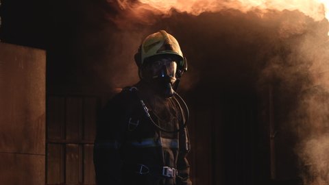 Fireman or fire fighter stand in front of big fire on wall of kitchen and heat show as vapor on his suit and he give sign to other people that no entry or go closer the dangerous.