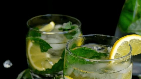 Slow motion Ice cube fall splash drops. Mojito refreshing cocktail, alcohol drink. Lemonade with lemon and mint leaves on dark background. Summer refreshing detox drinks. Clean eating, healthy