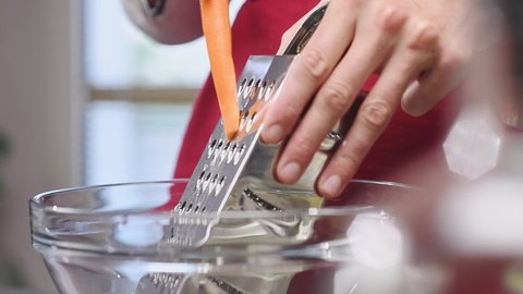 Grating fresh carrot with a grater in the kitchen.