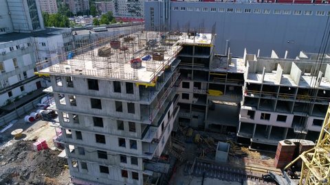 Movement from unfinished building. Workers are building a monolithic house and installation of reinforcing steel for concrete casting. Yellow tower crane and building materials at construction site.