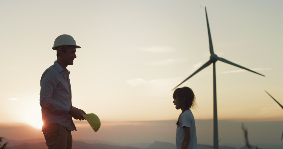 Wind Farm in Sunset: Male Engineer Putting a Protective Helmet on his Daughter's Head, Hugging Her, Giving Children the Clean Future They Deserve. Father Ensuring Kid's Dream for Sustainable Future Royalty-Free Stock Footage #1074587405