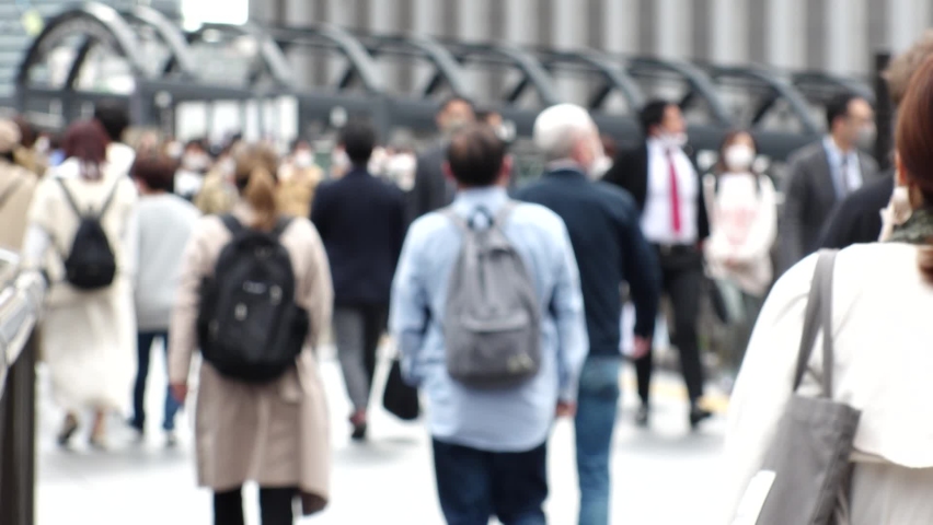 OSAKA, JAPAN - APRIL 2021 : Back shot and unidentified crowd of people wearing surgical masks to protect from Coronavirus (COVID-19) at the street near Osaka station. Slow motion shot. In front focus.