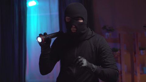 Portrait of a robber in a balaclava with a flashlight in the apartment