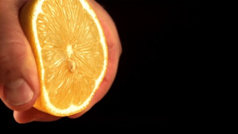 Super slow motion the man's hand squeezes the juice out of the fresh lemon. On a black background. Filmed on a high-speed camera at 1000 fps.