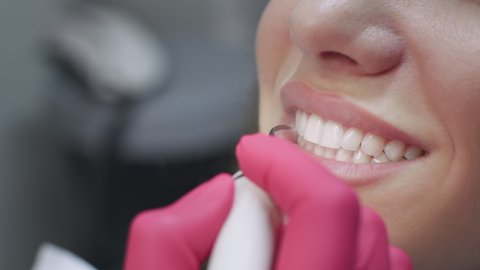 Professional teeth cleaning. Close up shot of doctor dentist making preventive deep cleaning procedure for female patient with perfect white smile at dental office, slow motion