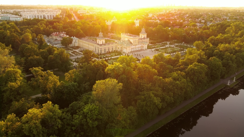 Drone aerial top view of the ancient royal castle palace with a park and a pond during a golden sunset. Historical place, tourist point spots of the city. Sunset, city on the horizon.