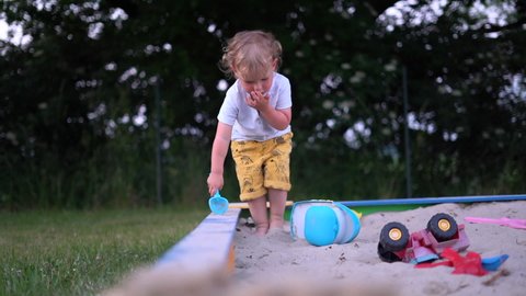 Cute blond kid playing in the sandbox with plastic toys alone. Happy childhood, children's leisure