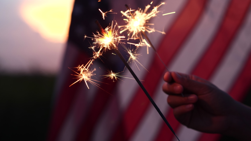 Happy 4th of July Independence Day. Hands holding sparklers celebration with American flag at sunset nature background, soft focus. Concept Independence,Memorial,Veterans, Celebrate,Fireworks,Labor.