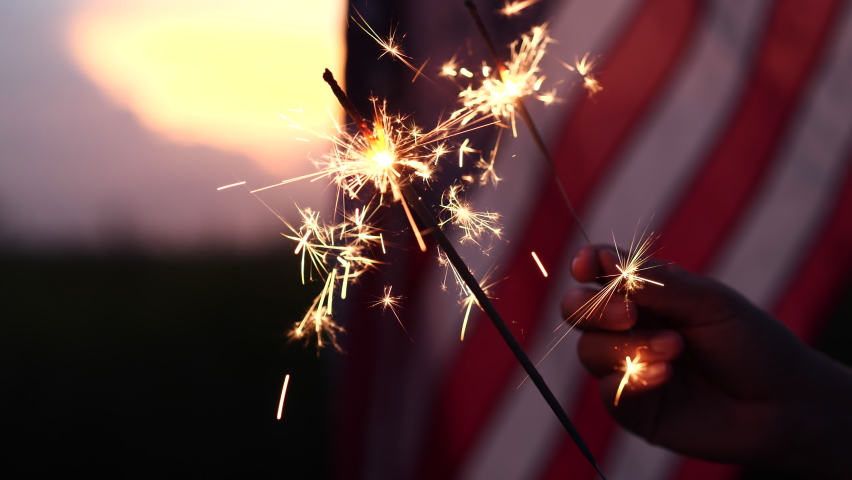 Happy 4th of July Independence Day. Hands holding sparklers celebration with American flag at sunset nature background, soft focus. Concept Independence,Memorial,Veterans, Celebrate,Fireworks,Labor.