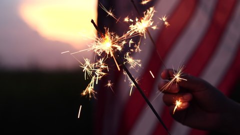 Happy 4th of July Independence Day. Hands holding sparklers celebration with American flag at sunset nature background, soft focus. Concept Independence,Memorial,Veterans, Celebrate,Fireworks,Labor.