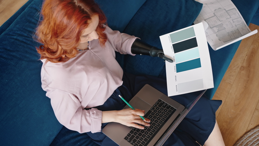 Top view of a girl interior designer with a bionic prosthesis is working on a project, typing text on a laptop, holding color reviews using a robotic hand. Royalty-Free Stock Footage #1074611453