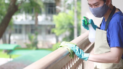 Young Asian male employee uses a towel soaked in alcohol to wipe off the railing or porch, Pathogen prevention or cleaning during virus outbreaks, Cleaning of a Building or office.