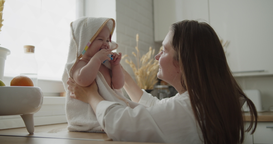 Mother and daughter spend time at home together. Young mom wipes her adorable little child after bathing in a kitchen sink. Woman holds adorable child wrapped in a towel. | Shutterstock HD Video #1074614813