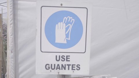 A light blue circle with the symbol of gloves are part of a sign displayed in the workplace. The sign says in Spanish "use guantes" which translates to "use gloves".