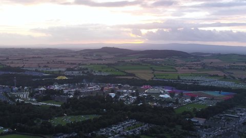 Aerial drone shot of large festival at sunset. Glastonbury, reading music festivals with camping and live music crowds.