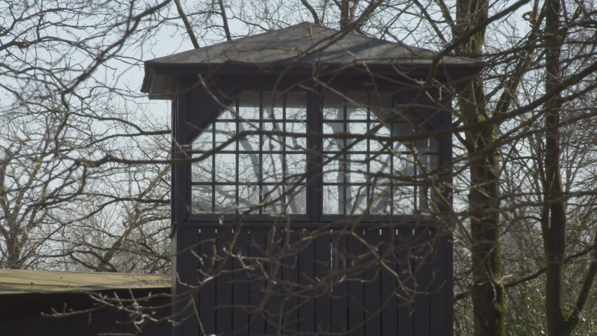 Dolly of concentration camp guard tower behind branches - close