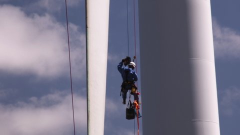 albany , Australia - 02 27 2021: Worker tied with the safety harness and hanging from high rise wind turbine