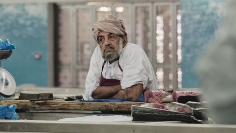 Muscat , Oman , Oman - 05 06 2018: Omani fishmonger leaning over Fish Market stall waiting for clients 