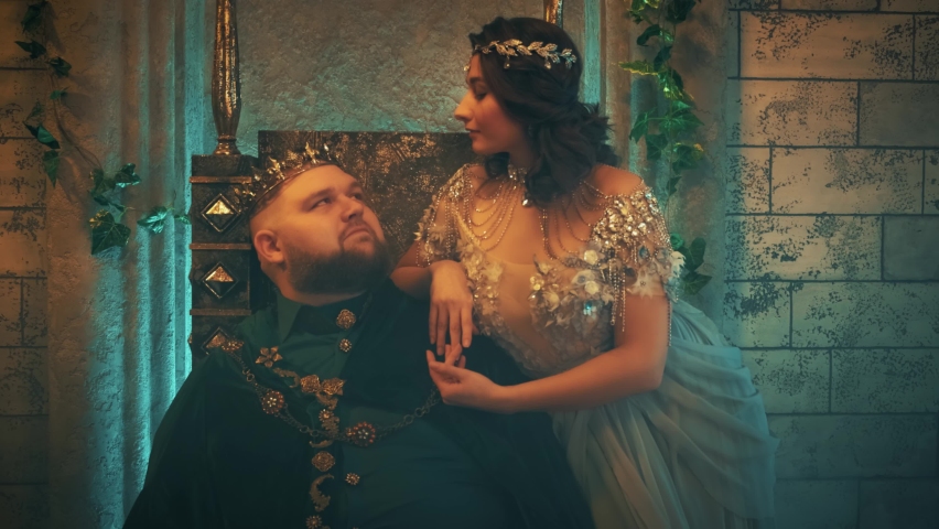 Fantasy clothing. art portrait woman medieval queen, stroking king husband man looking with love. royal couple family sits on throne. Vintage room gothic castle. jewelry crown men costume. blue dress 