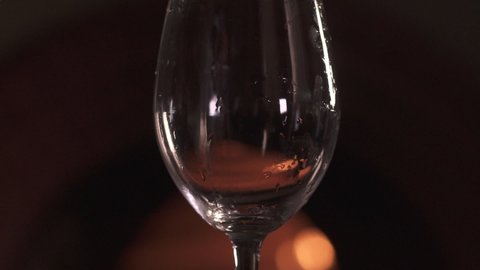 Close-up of a tall transparent glass in which white wine is poured in a dark room against the background of the fireplace.  Bokeh fire in the background. Slow motion 120 fps