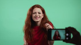 Smiling vlogger woman recording video of herself dancing in front of smartphone camera on green background. Influencer makes funny social media clip
