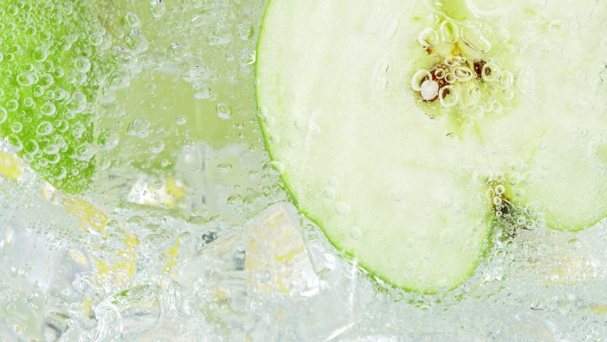 Super Slow Motion Shot of Fizzing Water with Apple Slices and Ice Cubes in Glass at 1000 fps.