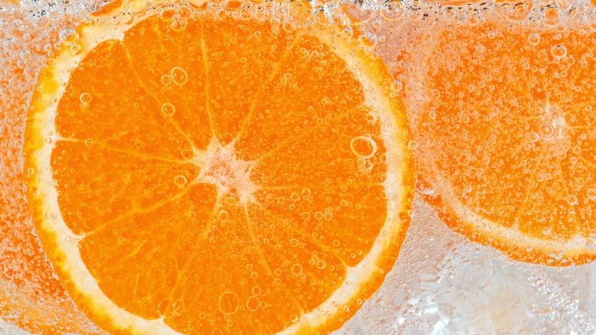 Super Slow Motion Shot of Fizzing Water with Orange Slices and Ice Cubes in Glass at 1000 fps.