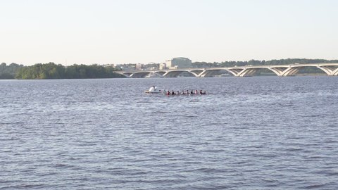 Alexandria, Virginia, USA- June 18th, 2021: A crew team rowing on the Potomac River with the Wilson Bridge and National Harbor in the background.