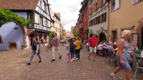 RIQUEWIHR, FRANCE - AUGUST 19, 2019: Tourists walk at around, enjoy old buildings and rest at restaurants. Couples and families visit beautiful Alsatian villages at the summertime.  