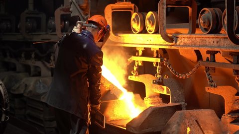a steelworker pours molten metal from a crucible into molds, the steel industry, a conveyor belt moves.
