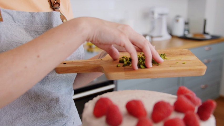 culinary, baking and cooking food concept - woman decorating raspberry cake with pistachio on kitchen at home
