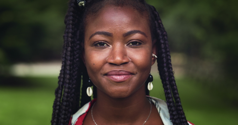 Close up Portrait of a Young Black Woman Looking at the Camera and Laughing in a Green Park . Pretty Female with Traditional African Braids and Accessories Enjoying Fresh Air and Nature