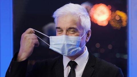 Businessman in suit smiles during covid 19 looks at camera. Elderly grey hair people at restrictions end. White old man takes face mask off. Portrait of elder gray gentlemen in coronavirus facemask.