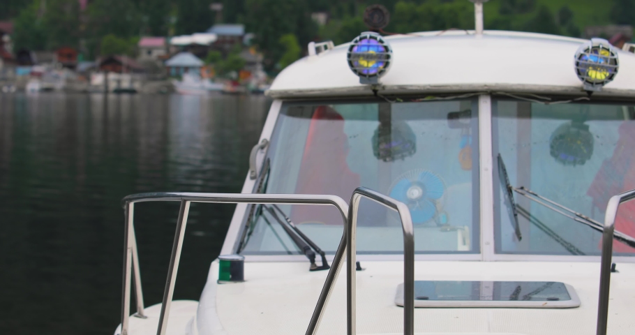 A high-speed snow-white boat stands on a pier on the lake. Only its front part is visible. It bobs gently on the waves. Another boat passes in the background. It makes waves on the water.