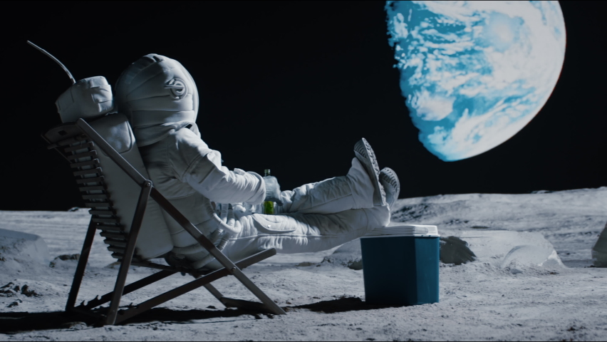 Back view of lunar astronaut opens a beer bottle while resting in a beach chair on Moon surface, enjoying view of Earth. Shot with 2x anamorphic lens Royalty-Free Stock Footage #1074659972