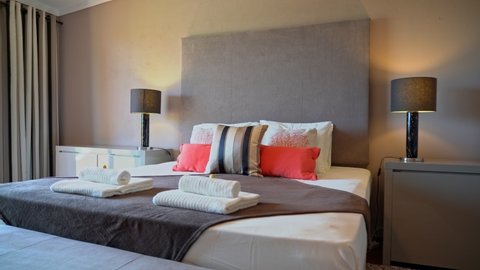 Cozy modern bedroom with a bed in a hotel, home for rest, sleep. Folded towels. Bedside tables with table lamps.