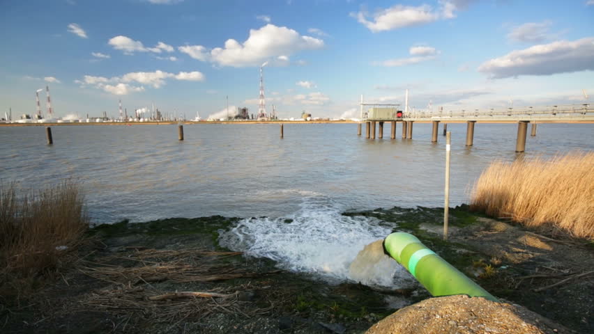 A wastewater pipe and a large oil refinery in the harbor of Antwerp, Belgium with blue sky and warm evening light.