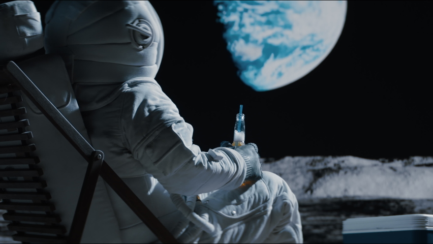 Back view of lunar astronaut having a beer while resting in a beach chair on Moon surface, saluting to Earth. Shot with 2x anamorphic lens Royalty-Free Stock Footage #1074664769